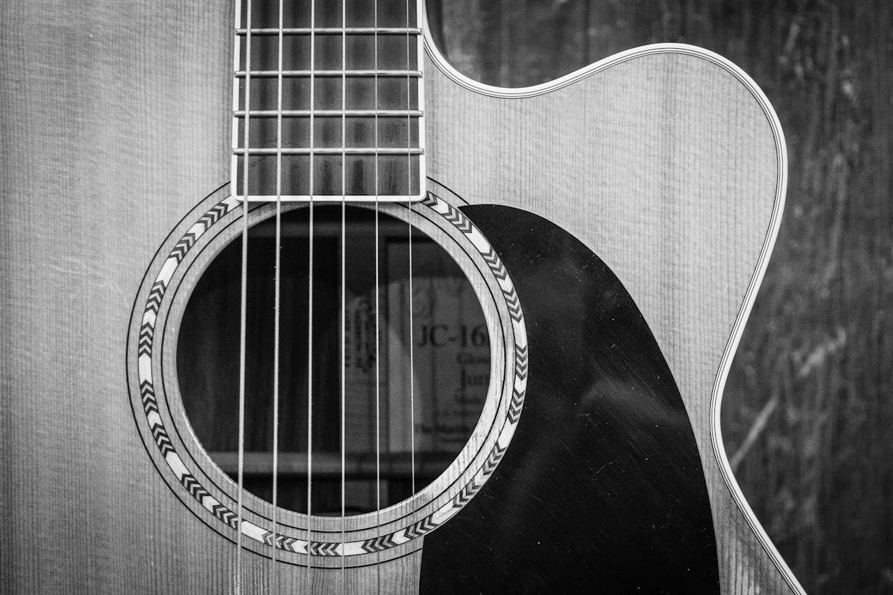 our-story Detailed black and white photo of an acoustic guitar showcasing strings and sound hole.