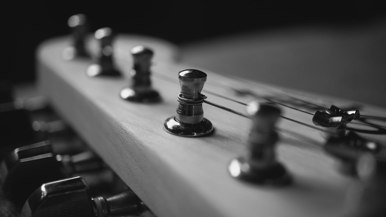 why-choose-us Black and white close-up of guitar headstock with tuning pegs.