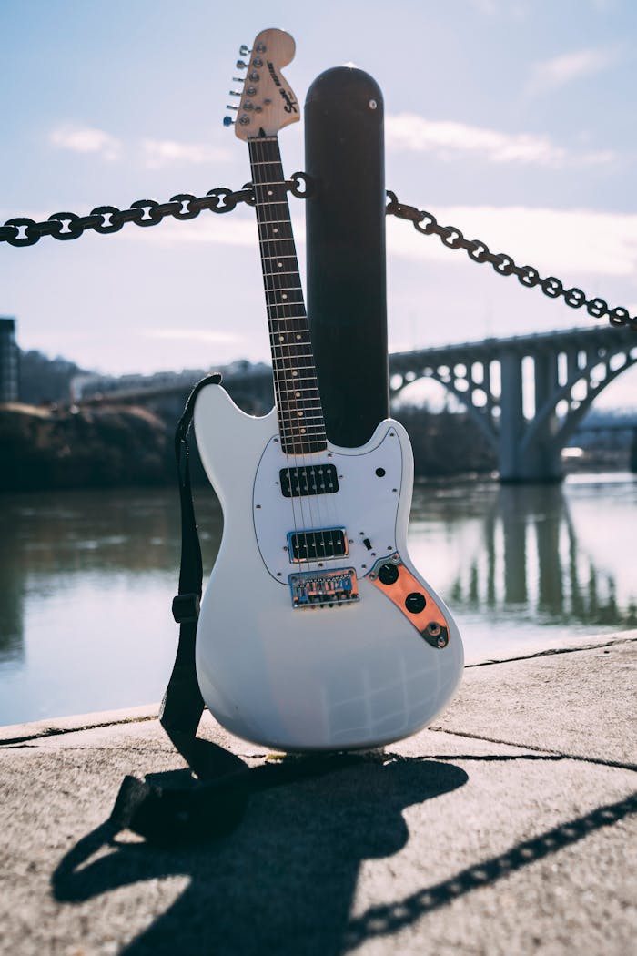 Crafting Captivating Headlines: Your awesome post title goes here Electric guitar resting by the riverside with a bridge in the background, under daylight.