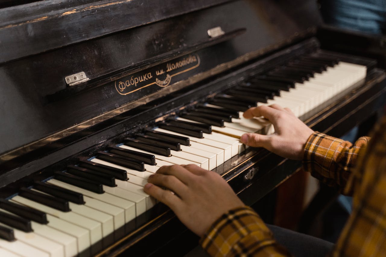 about-us Close-up of hands playing a vintage piano with Russian brand label in a cozy indoor setting.